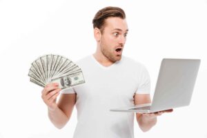 shocked young man holding money using laptop computer 1